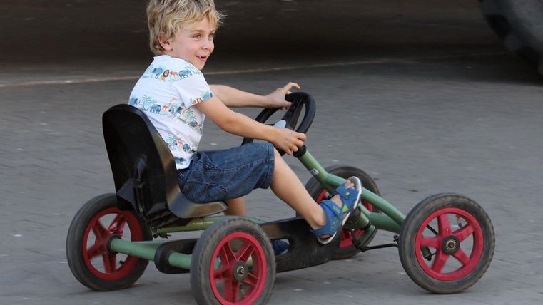 Ein Junge fährt fröhlich auf einem Gokart. Die Umgebung scheint eine Spiel- oder Freizeitfläche zu sein.