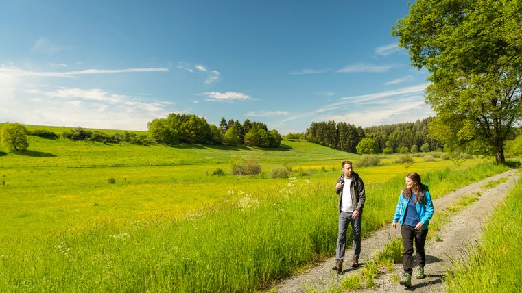 Twee wandelaars op een pad in het Murmes natuurreservaat, omringd door groene weiden en bomen onder een blauwe hemel.