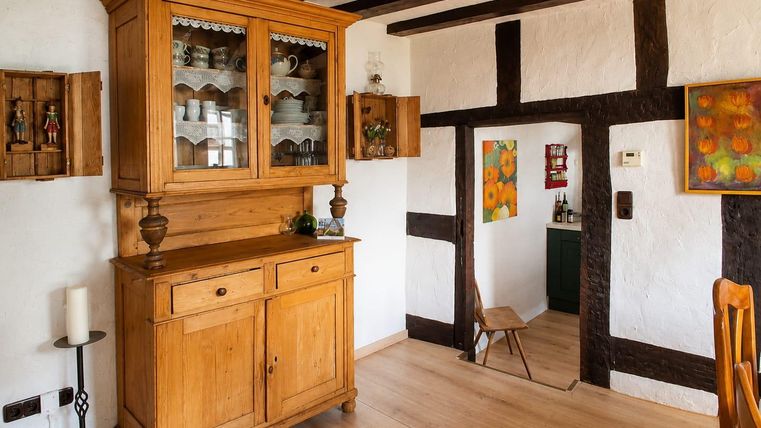 Ein gemütlicher Raum mit einem Holzschrank und einem hellen Fuβboden. An den Wänden hängen bunte Bilder und es gibt einen Zugang zu einer weiteren Ecke des Raumes.