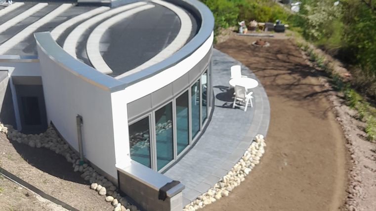 Ein modernes Haus mit einer geschwungenen Fassade und großen Fenstern. Umgeben von einer grünen Landschaft und einem angelegten Garten.