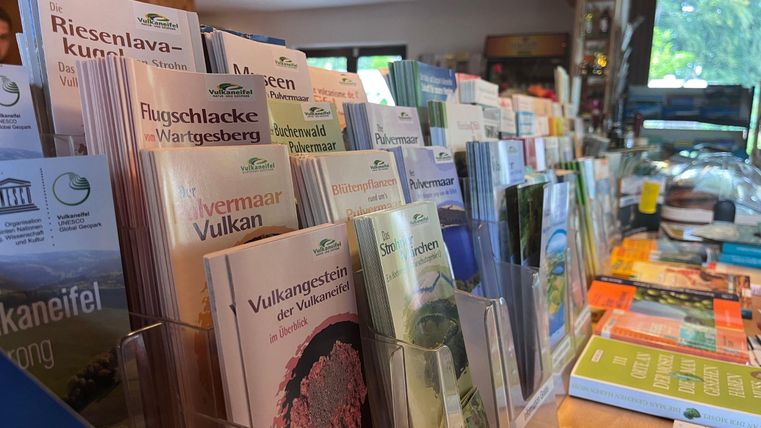 Ein Tisch mit verschiedenen Informationsflyern und Broschüren über Natur und Wanderziele. Die Gegend wirkt einladend und informativ.