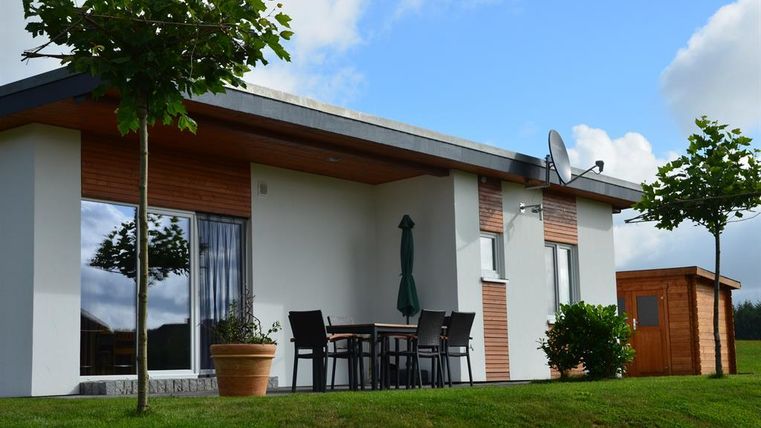Ein modernes Haus mit einem begrünten Garten. Vor dem Haus steht ein Tisch mit Stühlen und ein kleiner Gartenhaus.