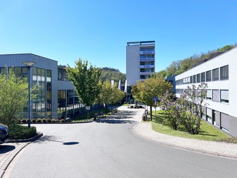 Moderne Gebäude mit klaren Linien und grünem Bereich. Bäume und Gemeinschaftsflächen schaffen eine einladende Atmosphäre.