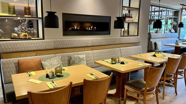 Ein modernes Restaurant mit Holzstühlen und Tischen. Gemütliche Beleuchtung und eine einladende Atmosphäre schaffen einen angenehmen Essbereich.