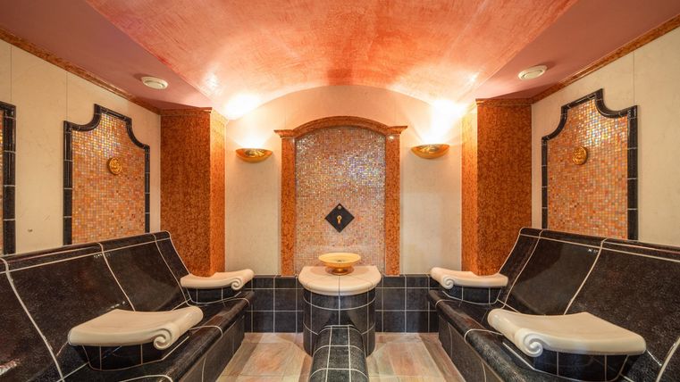 Ein eleganter Wellnessraum mit eleganten Liegen und sanfter Beleuchtung. Die Wände sind mit stilvollen Fliesen und Holzverzierungen gestaltet.