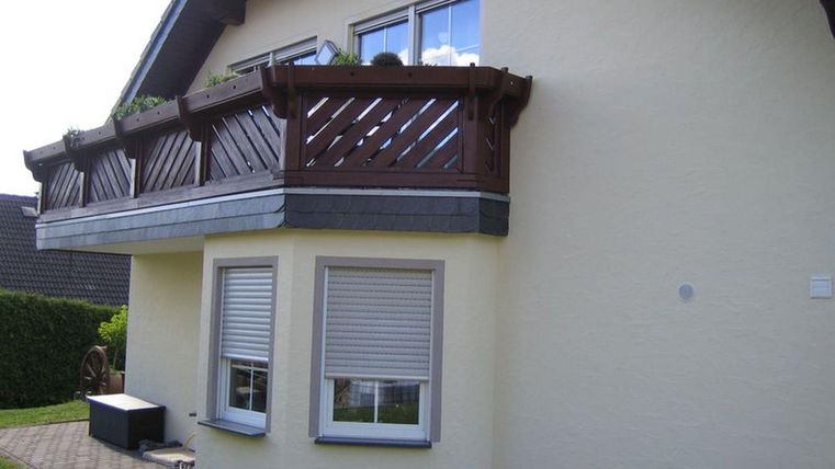 Ein modernes Haus mit einem Balkon aus Holz. Die Fassade ist gelb und das Grundstück hat einen gepflegten Garten.