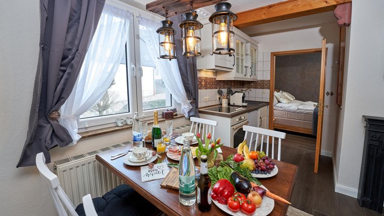 Ein einladender Esstisch mit frischen Früchten und Getränken in einer gemütlichen Küche. Die Fenster sind mit Vorhängen geschmückt, und die Atmosphäre ist warm und einladend.