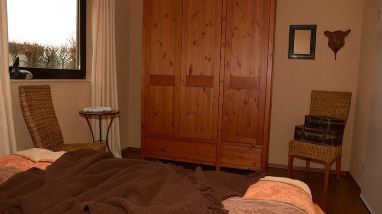 Ein gemütliches Schlafzimmer mit einem Holzschrank und zwei Stühlen. Das Bett ist mit einer braunen Decke und bunten Kissen dekoriert.