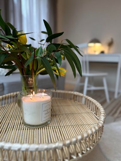 Ein stilvoller Tisch mit einer Kerze und einer Vase mit frischen Blumen. Im Hintergrund ist ein heller Raum mit einem Schreibtisch sichtbar.