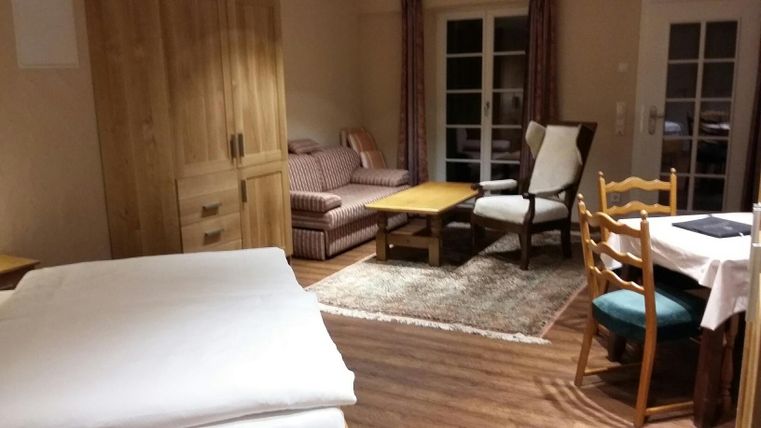Ein gemütliches Zimmer mit Holzmöbeln und einem großen Fenster. Es gibt ein Bett, eine Sitzecke und einen Esstisch.