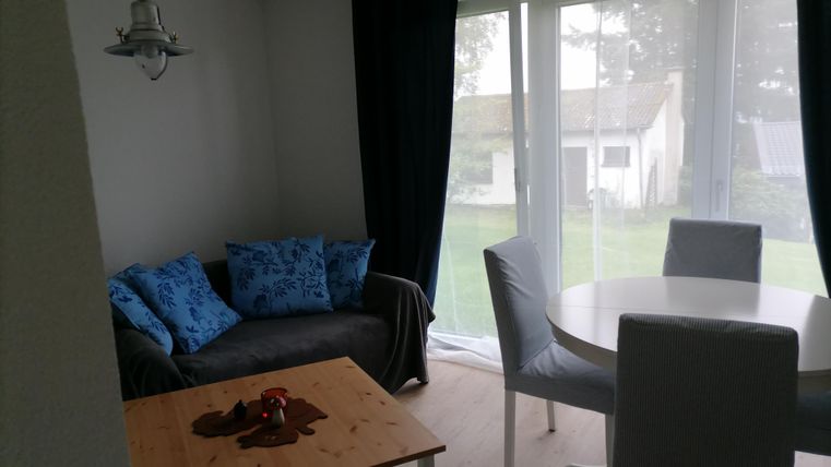 Ein gemütlicher Wohnbereich mit einem Sofa und Tisch. Große Fenster bieten Blick auf den Garten.