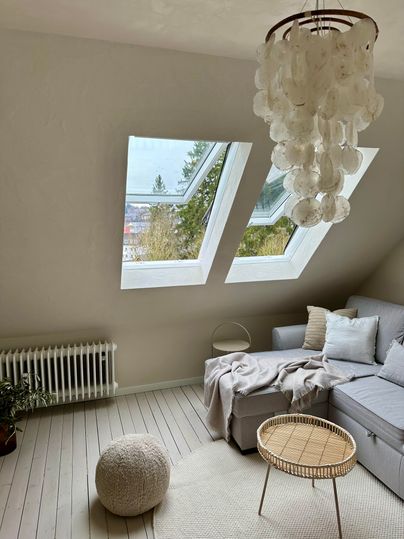 Ein helles, modernes Wohnzimmer mit Dachfenstern und einer gemütlichen Couch. Ein runder Tisch und ein weicher Teppich ergänzen die einladende Atmosphäre.