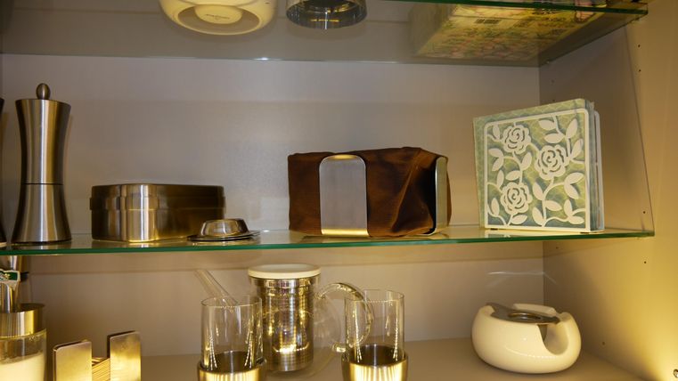 Ein Regalsystem mit verschiedenen Küchenutensilien und dekorativen Gegenständen. Darunter befinden sich Gläser, eine Teekanne und ein elegantes Dekorationsbuch.