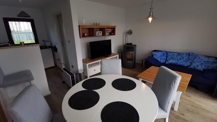 Ein gemütlicher Wohnbereich mit einem runden Esstisch, Stühlen und einer blauen Couch. Der Raum hat helle Wände und einen Holzfußboden, wodurch er freundlich wirkt.
