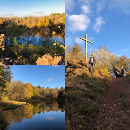 Eine schöne Landschaft mit Seen und herbstlichen Bäumen. Im Hintergrund steht ein Kreuz auf einem Hügel unter klarem Himmel.