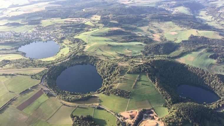 Eine beeindruckende Landschaft mit zwei großen Seen und umgebenden Wiesen und Feldern. Im Hintergrund sind sanfte Hügel und ein klarer Himmel zu sehen.