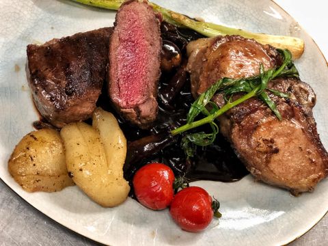 Ein köstlicher Teller mit zartem Fleisch, das rosa gebraten ist. Dazu gibt es Kartoffeln, Kirschtomaten und eine grüne Garnitur.