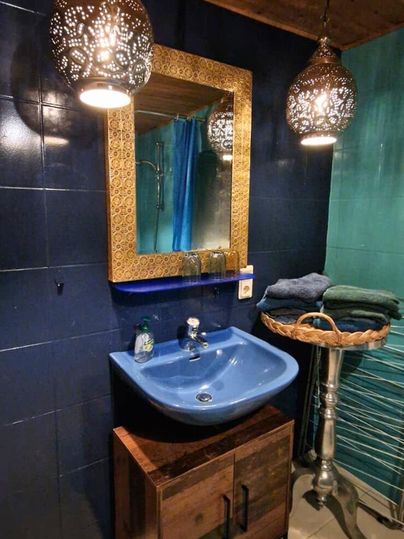 Ein stilvolles Badezimmer mit einer blauen Waschschüssel und einem schönen Spiegel. Deckenleuchten und eine grüne Wand verleihen dem Raum eine gemütliche Atmosphäre.