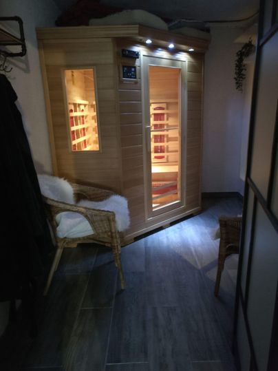Eine gemütliche Sauna in einem modernen Raum, ausgestattet mit einer Holzbank und indirekter Beleuchtung. Daneben stehen zwei Stühle für Entspannung.
