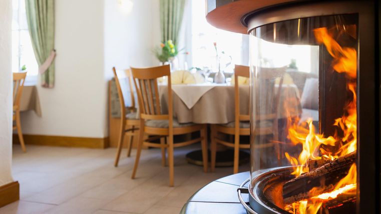 Ein gemütlicher Restaurantbereich mit einem offenen Kamin. Flackerndes Feuer und ein einladendes Ambiente schaffen eine warme Atmosphäre.