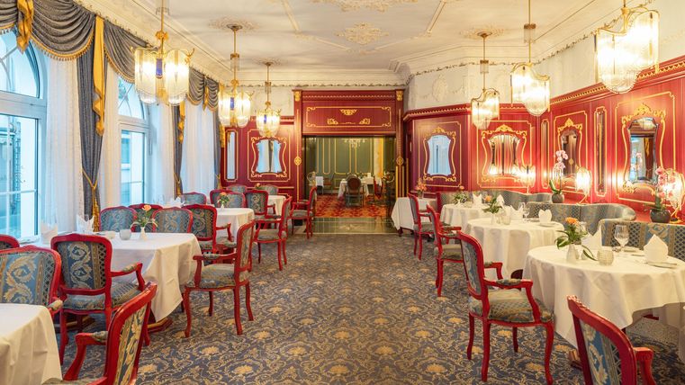 Ein elegantes Restaurant mit roten Wänden und stilvollen Möbeln. Die Tische sind liebevoll gedeckt und die Beleuchtung ist warm und einladend.