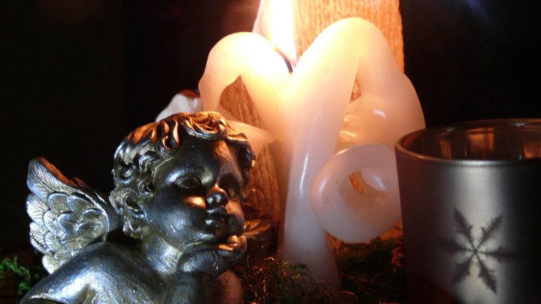 Eine dekorative Szene mit einer Engel-Statue, einer Kerze und Weihnachtsdekoration. Die Atmosphäre ist warm und festlich.
