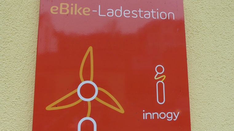 Ein rotes Schild mit der Aufschrift "eBike-Ladestation". Es zeigt ein Symbol für eine Windkraftanlage und das Logo von innogy.