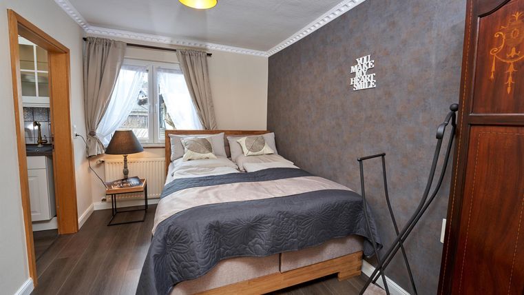 Ein gemütliches Schlafzimmer mit einem Doppelbett und dekorativen Kissen. Die Wände sind in sanften Farben gehalten, und es gibt einen kleinen Tisch sowie einen Kleiderschrank.