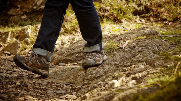 Eine Person geht auf einem unebenen, steinigen Weg. Die Wanderschuhe sind stabil und geeignet für das Gelände.