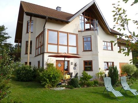 Ein modernes Haus mit großen Fenstern und einem bepflanzten Garten. Zwei Liegen stehen auf der Rasenfläche für Entspannung.