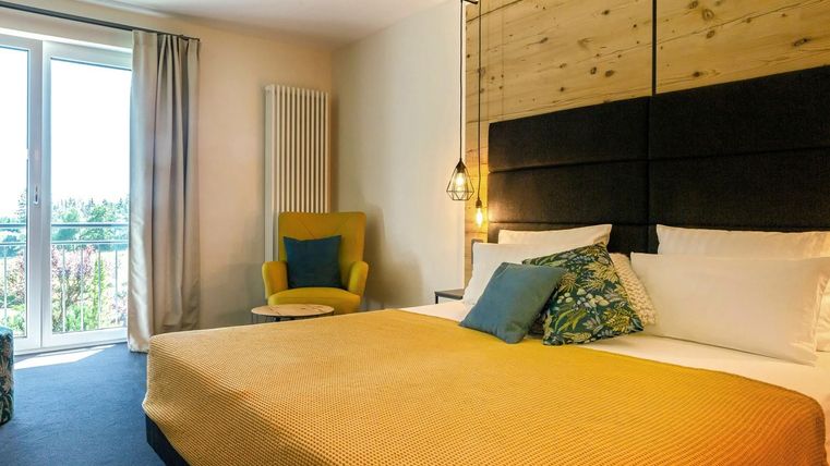 Ein komfortables Zimmer mit einem großen Bett und einer gemütlichen Sitzecke. Die Fenster lassen viel Licht herein und bieten einen Blick nach draußen.