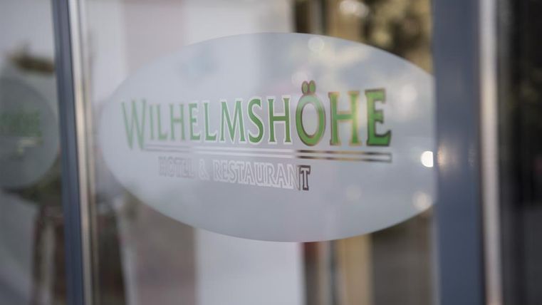 Ein transparentes Schild mit der Aufschrift „WILHELMSHÖHE“. Es zeigt, dass es sich um ein Restaurant handelt.