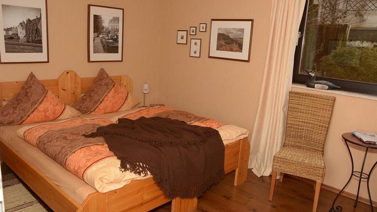 Ein gemütliches Schlafzimmer mit einem großen Bett und dekorativen Kissen. An den Wänden hängen Bilder und ein Stuhl steht neben dem Fenster.